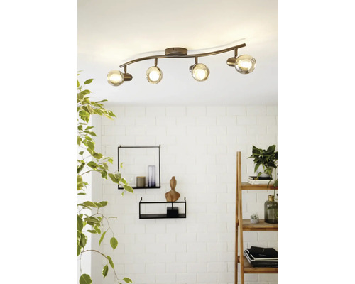 Plafonnier avec quatre spots et abat-jour en verre sur une barre incurvée.