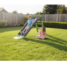 Un garçon glisse sur un toboggan pour enfants dans le jardin, tandis qu'une fille regarde