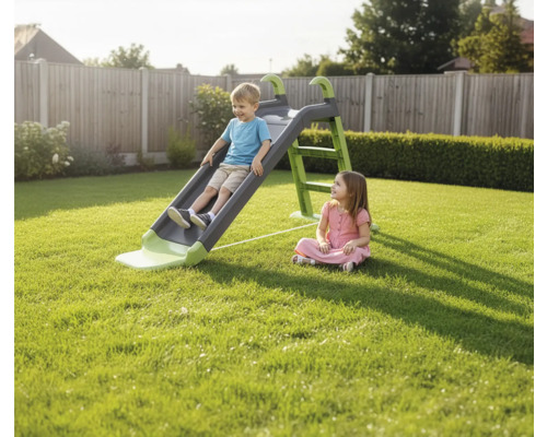 Un garçon glisse sur un toboggan pour enfants dans le jardin, tandis qu'une fille regarde