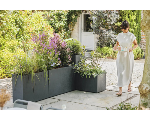 Gartenansicht mit grauen Pflanzgefäßen und einer Frau, die ein Tablett trägt