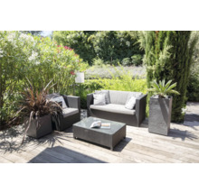 Gartenszene mit Sitzgruppe, bestehend aus Sofa, Sessel und Tisch, sowie Pflanzen in Pflanzkübeln auf einer Holzterrasse