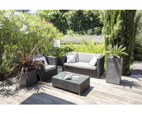 Gartenszene mit Sitzgruppe, bestehend aus Sofa, Sessel und Tisch, sowie Pflanzen in Pflanzkübeln auf einer Holzterrasse