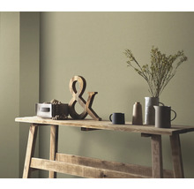 Scène décorative sur une table en bois avec une décoration en bois, des fleurs séchées dans un vase et de la vaisselle en céramique devant un mur coloré.