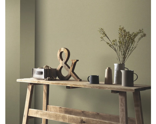 Scène décorative sur une table en bois avec une décoration en bois, des fleurs séchées dans un vase et de la vaisselle en céramique devant un mur coloré.