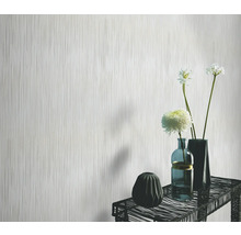 Papier peint clair avec motif à rayures verticales devant une table avec des vases et des fleurs