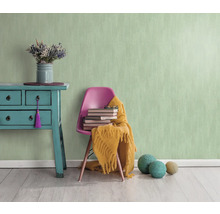 Pièce lumineuse avec papier peint structuré vert menthe, commode, chaise, livres et décoration