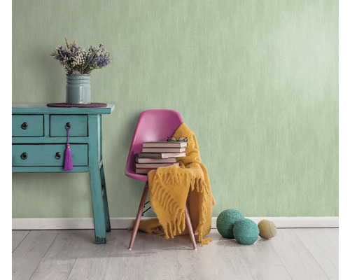 Pièce lumineuse avec papier peint structuré vert menthe, commode, chaise, livres et décoration