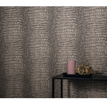 Gros plan d'un mur avec du papier peint imitation cuir de reptile, un plateau à bougies avec une bougie et une décoration florale