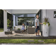Ein moderner Terrassenbereich mit grauen Polyrattan-Gartenmöbeln, einer weißen Regentonne mit Pflanzgefäß und zwei Personen.