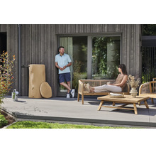 Récupérateur d'eau de pluie aspect tronc d'arbre à côté de meubles de jardin en bois sur une terrasse moderne en lames grises.