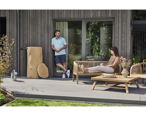 Récupérateur d'eau de pluie aspect tronc d'arbre à côté de meubles de jardin en bois sur une terrasse moderne en lames grises.