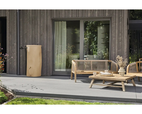 Récupérateur d eau de pluie beige sur une terrasse moderne avec des meubles de jardin en bois et une façade grise.