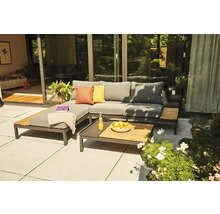Salon de jardin moderne sur une terrasse avec canapé d angle gris, éléments en bois et table basse assortie devant une baie vitrée.
