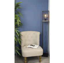 Sessel mit Buch und Brille neben Stehlampe und Zimmerpflanze