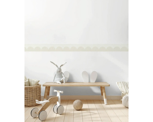 Helles Kinderzimmer mit Tapetenbordüre im Wellendesign an der Wand. Holzbank, Laufrad aus Holz und Weidenkorb auf hellem Holzboden.