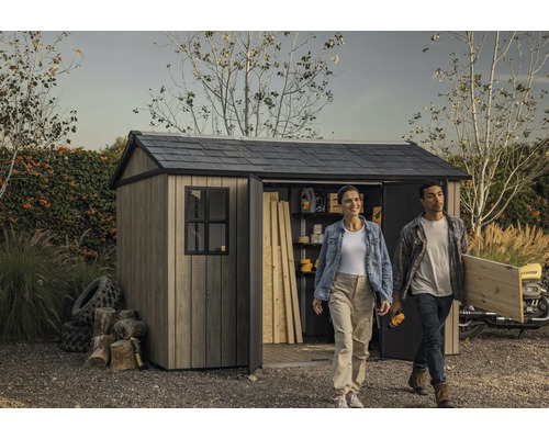 Gartenszene mit Gerätehaus, einer Frau und einem Mann, die Werkzeuge und Holz tragen