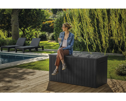 Gartenszene mit einer Frau, die auf einer grauen Gartenbox aus Kunststoff neben einem Pool sitzt.