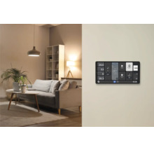 Écran mural domotique pour contrôler l'éclairage et la température dans un salon moderne avec canapé et lampes.