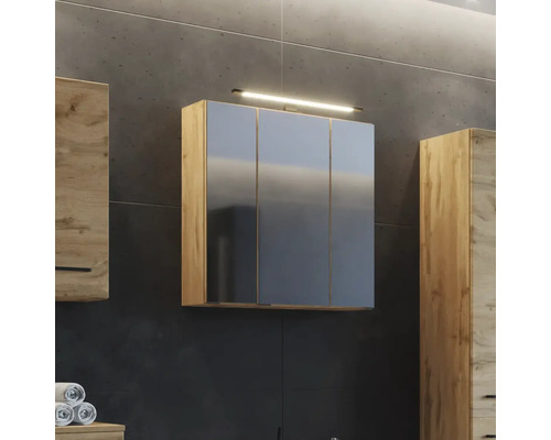 Dreitüriger Spiegelschrank in Eichenoptik mit Beleuchtung an einer dunklen Wand im Badezimmer neben weiteren Badmöbeln aus Holz.
