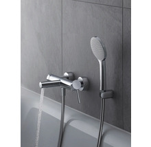 Aufnahme einer verchromten Badewannenarmatur mit Duschkopf an einer grauen Wand, Wasser läuft aus dem Wasserhahn.