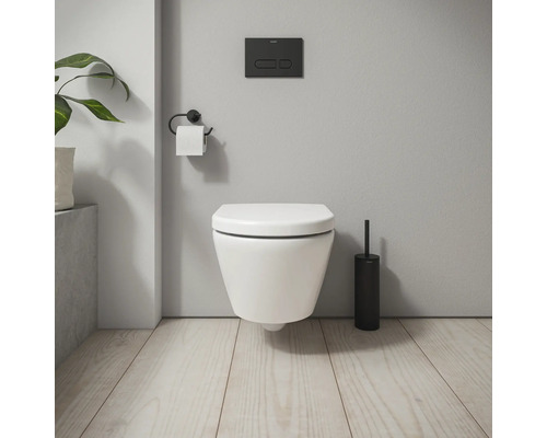 Wandhängendes WC mit Betätigungsplatte, Toilettenpapierhalter und Toilettenbürste in einem Badezimmer.