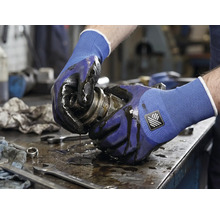 Une personne tenant un composant mécanique huileux avec des gants de travail.