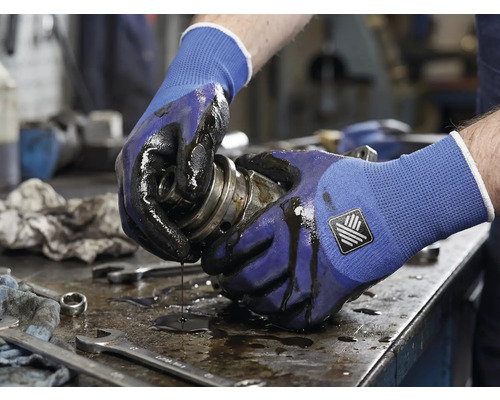 Une personne tenant un composant mécanique huileux avec des gants de travail.