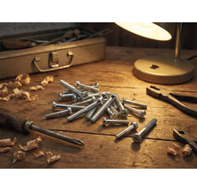 Scène d'atelier avec vis, tournevis, pince, copeaux de bois, boîte à outils et lampe sur une table en bois