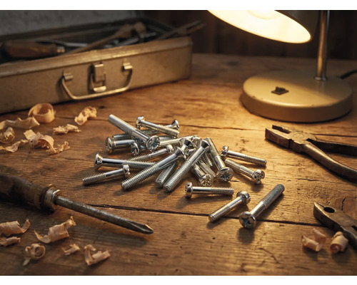 Scène d'atelier avec vis, tournevis, pince, copeaux de bois, boîte à outils et lampe sur une table en bois
