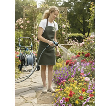 Une femme arrose des fleurs avec un tuyau d'arrosage dans un jardin luxuriant avec une tonnelle de roses