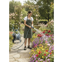 Femme arrosant des fleurs avec un tuyau d'arrosage à côté d'un chariot à tuyau dans un jardin fleuri.