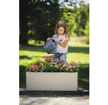 Mädchen giesst Blumen in einem rechteckigen Pflanzkasten im Garten.