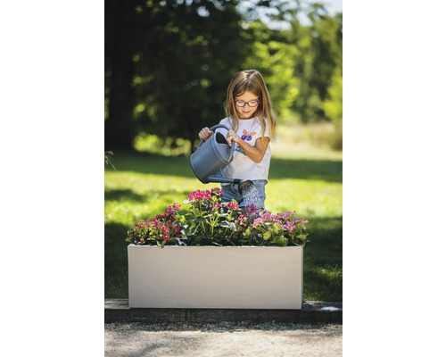 Mädchen giesst Blumen in einem rechteckigen Pflanzkasten im Garten.