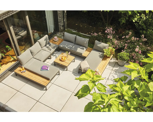 Loungegruppe aus Holz und grauem Polster auf einer Terrasse, kombiniert mit einem Holztisch und grüner Vegetation.