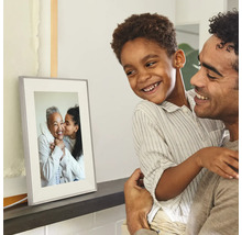Cadre photo numérique sur une étagère, regardé par un père et son fils souriants.