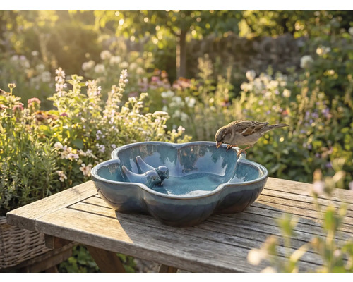 Vogeltränke aus Keramik mit Vogeldekoration auf Holztisch im Garten