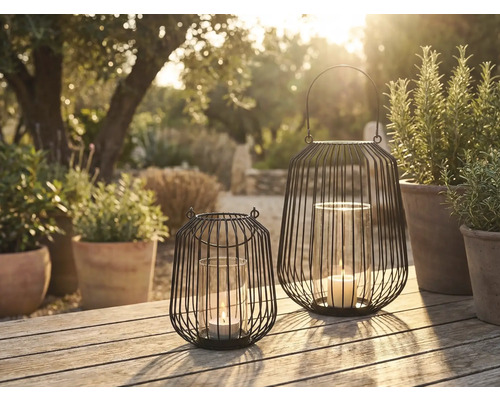 Zwei dekorative Windlichter aus Metall mit Glaseinsatz und Kerze auf einem Gartentisch