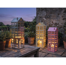 Drei dekorative Windlichter in Gebäudeform mit Kerzen auf einem Gartentisch