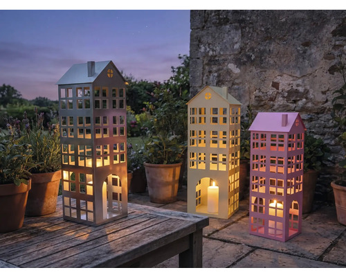 Drei dekorative Windlichter in Gebäudeform mit Kerzen auf einem Gartentisch