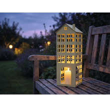 Windlicht in Hausform mit Kerze auf einer Holzbank im Garten