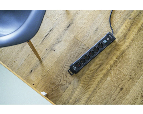 Mehrfachsteckdose auf einem Holzboden neben einem Stuhl.