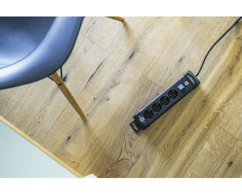 Steckdosenleiste mit Überspannungsschutz und Schalter auf Holzboden.