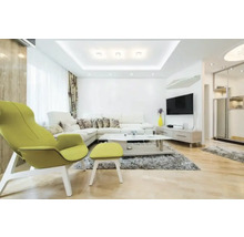 Salon moderne et lumineux avec canapé d'angle blanc, fauteuil vert citron avec repose-pieds, table basse blanche sur tapis gris et téléviseur mural.
