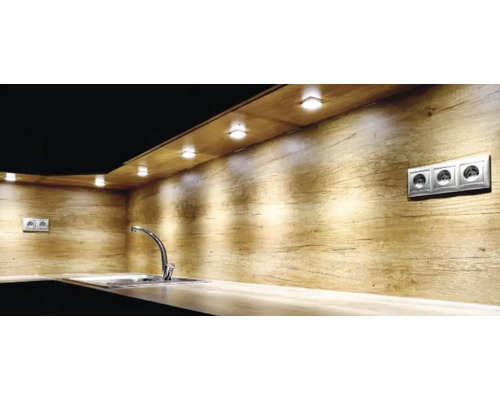 Cuisine moderne avec paroi arrière imitation bois, des spots LED sous meuble éclairent un plan de travail avec évier et robinet chromé.