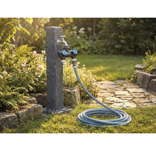Gartenszene mit Wasserhahn, Verteiler und Gartenschlauch auf einem Rasen