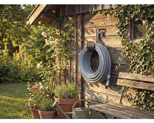 Scène de jardin avec enrouleur de tuyau sur mur en bois, entouré de plantes