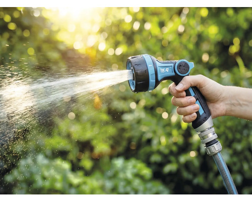 Eine Hand hält eine Gartenspritze mit Wasserstrahl vor einem grünen Hintergrund.