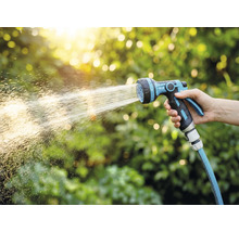 Eine Hand hält einen Gartenschlauch mit Spritzpistole, der Wasser verspritzt.