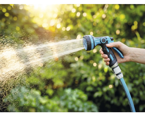 Eine Hand hält einen Gartenschlauch mit Spritzpistole, der Wasser verspritzt.