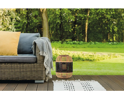 Scène de jardin avec lanterne en rotin, canapé d'extérieur et tapis sur une terrasse en bois